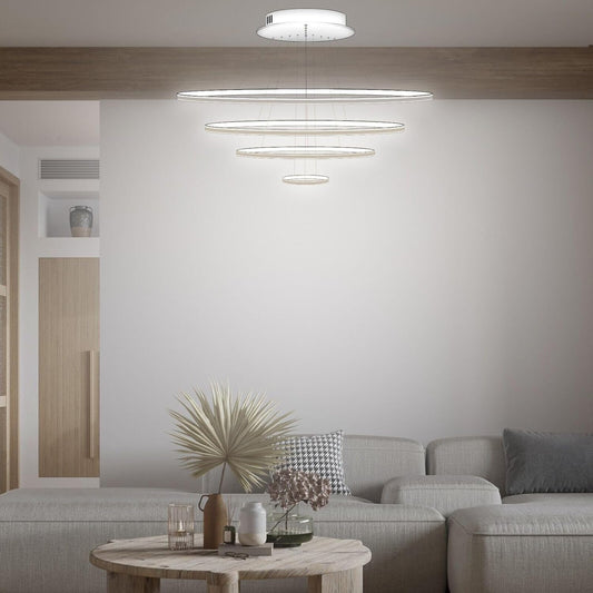 Lampadario LED MAKA con quattro cerchi sospesi in ordine decrescente, bianco trasparente, sopra divano grigio in salotto moderno.
