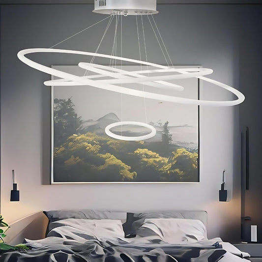 Lampadario sospeso con quattro cerchi luminosi bianchi in metallo sopra un letto grigio.